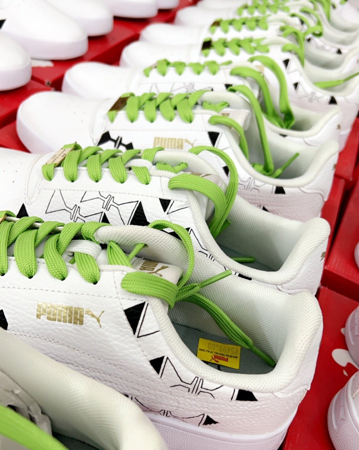 Row of white sneakers with green laces on a red surface