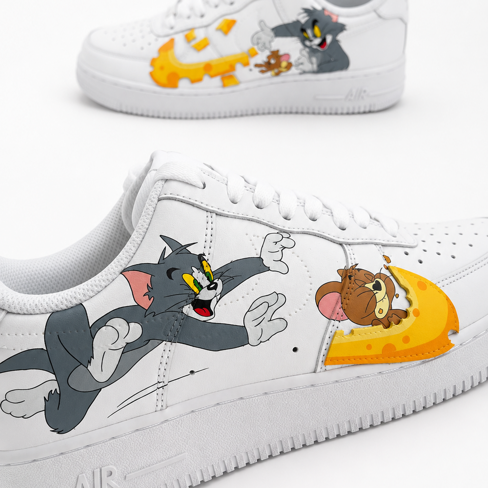 A pair of white low-top sneakers featuring cartoon graphics of Tom and Jerry running alongside a large yellow cheese wheel. The shoes are shown from multiple angles against a clean white background.