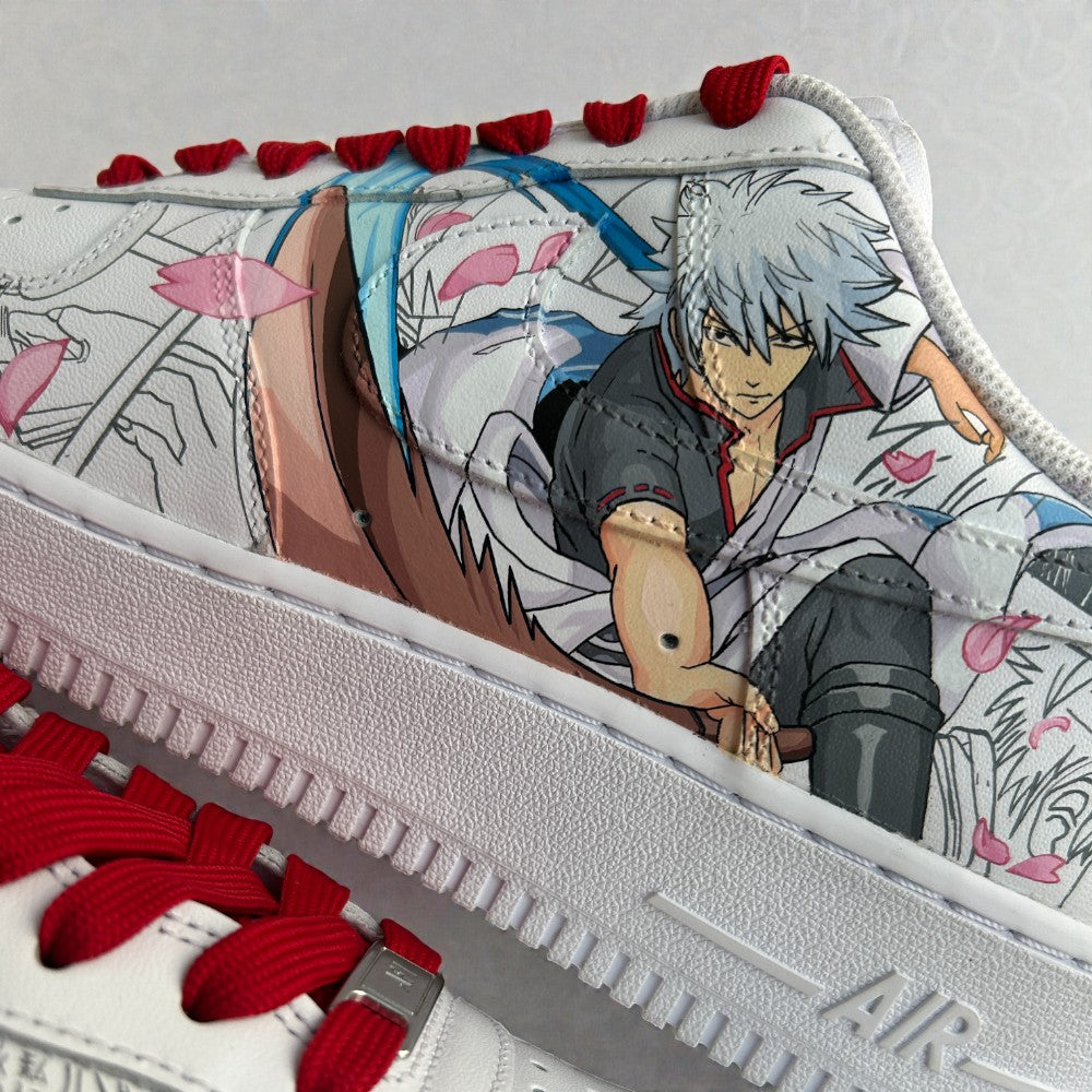 Close-up detail of custom hand-painted Nike Air Force 1 sneakers featuring anime character illustration layered over manga line art, accented with red laces, cherry blossom elements, and fine brushwork on premium white leather.