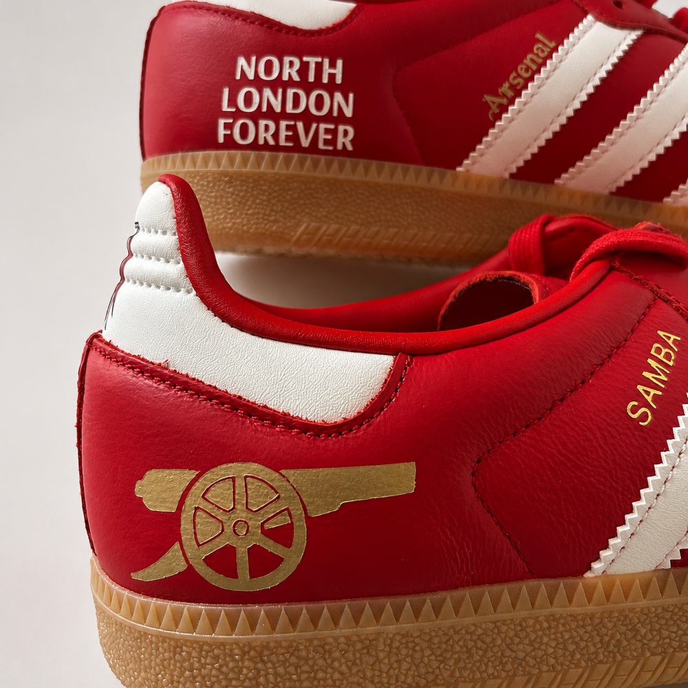 A pair of red low-top Adidas red samba sneakers featuring Arsenal icons. 