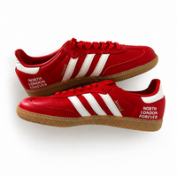 A pair of red Adidas Samba sneakers, styled as a flat-lay on a clean white background. The shoes feature red leather uppers with three white stripes, a brown gum sole, and 'NORTH FOREVER' text printed on the side and heel.
