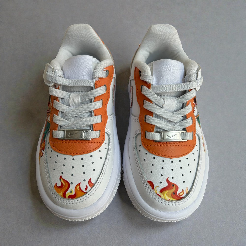 Top view of custom hand-painted kids Nike Air Force 1 sneakers featuring orange leather accents, flame artwork on the toe box, white perforated leather panels, and classic lace-up detailing.