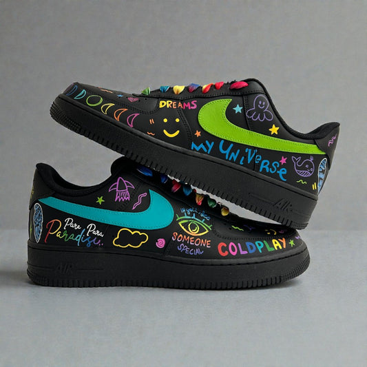 Hand-painted black Air Force 1 custom sneakers inspired by Coldplay, featuring colourful doodle art, lyric text, moon and star motifs, neon green swoosh, and rainbow laces.