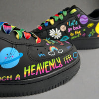 Close-up of black custom Nike Air Force 1 sneakers with rainbow laces, hand-painted doodles, planets, flowers, and colourful text reading “Heavenly Feel”.