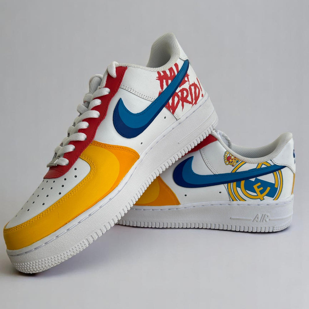 A pair of custom AF1 sneakers hand-painted in white, gold, red, and blue with the Real Madrid crest.