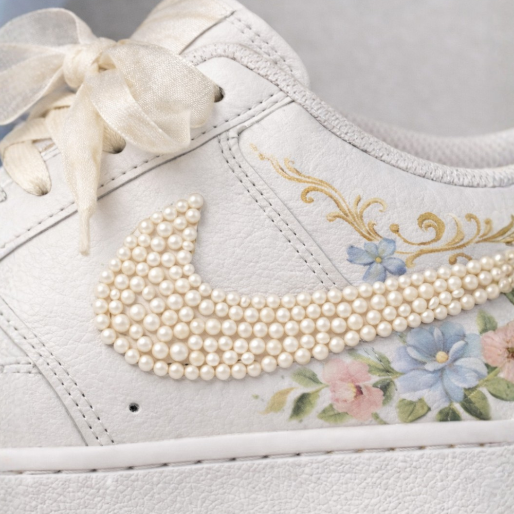 White sneaker with floral design and pearl embellishments on the Nike logo.