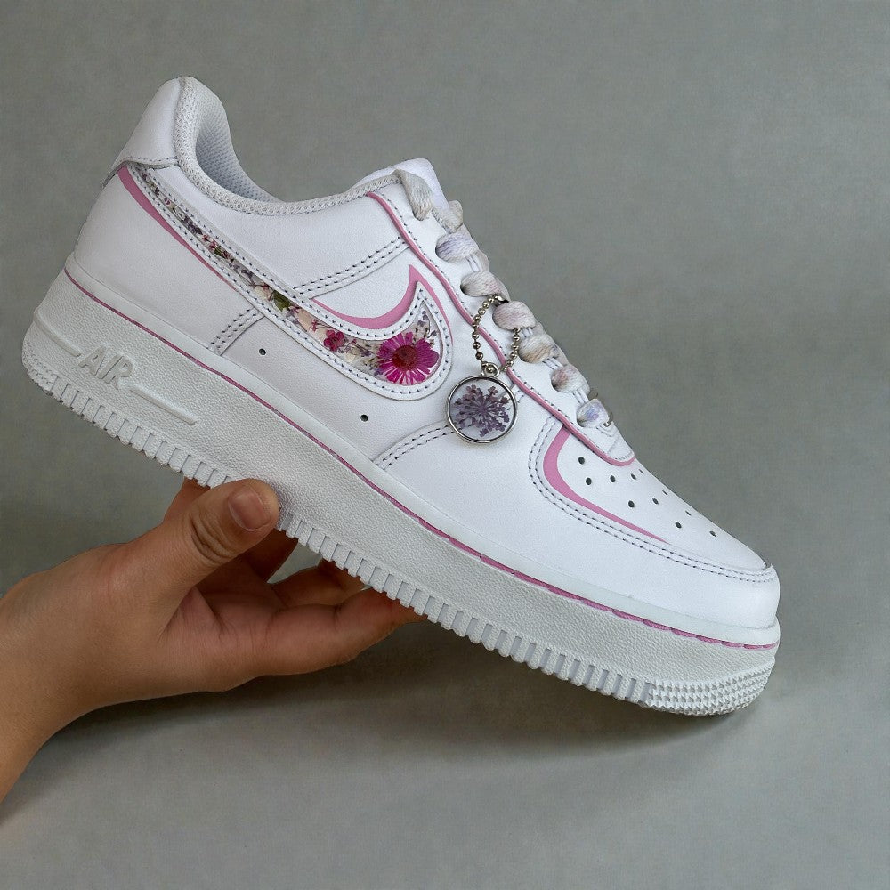 White sneaker with pink accents held by a hand on a gray background