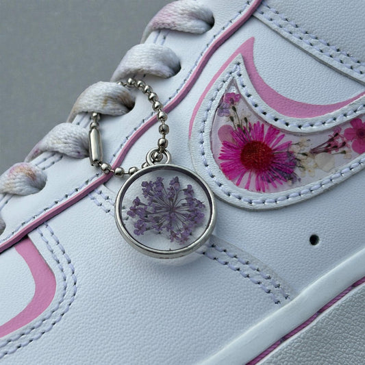White sneaker with pink floral design and a purple flower charm on a gray background